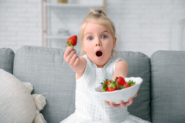 Wall Mural - Surprised little girl showing delicious strawberry in living room