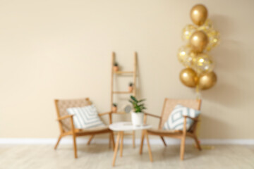 Sticker - Beautiful golden air balloons with chairs and coffee table near beige wall at home, blurred view