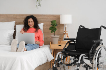 Poster - Young African-American woman with wheelchair and laptop lying on bed at home