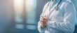 © Naret - Doctor in white coat with stethoscope, hands clasped, standing in modern medical facility with soft lighting and blurred background.