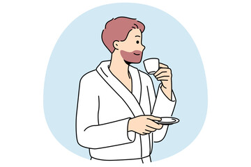 Man in bathrobe drinks coffee enjoying hot tart drink after waking up in morning. Successful young man with tea having rest in hotel or using services of spa center during vacation or weekend