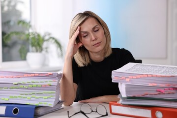 Canvas Print - Overwhelmed woman sitting at table with stacks of documents and folders in office