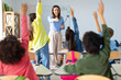 © Home-stock - Students raising their hands up in classroom at international elementary school. Cheerful female teacher playing with pupils