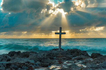 A cross on a rocky shoreline, with sunrays shining through dramatic ocean clouds, casting light over the waves.