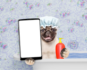 Aufkleber - Happy Mastiff puppy wearing shower cap with cream on it face takes the bath and holds bottle of shampoo, shows big smartphone with white blank screen in it paw. Empty space for text