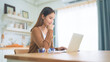 © Monster Ztudio - Beautiful young Asian woman working with laptop computer in home kitchen. Work at home