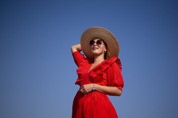 Wall Mural - A woman in a red dress and straw hat is smiling and looking up at the sky