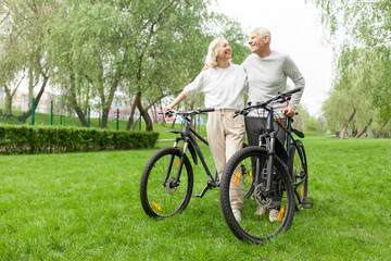 elderly senior couple rides bicycle in the park in the summer and smiles, old gray-haired man and woman are actively resting outdoors, old people practice cycling in forest