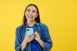 © Ivan - Young adult smiling happy pretty woman holding mobile phone device using apps on cellphone standing isolated on yellow background.