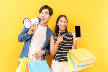 Young Asian couple enjoying a day of shopping, holding paper bags, set against a bright yellow backdrop