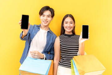 Young Asian couple enjoying a day of shopping, holding paper bags, set against a bright yellow backdrop