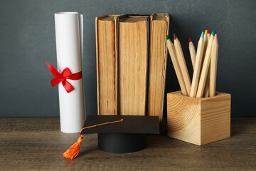 Wall Mural - Graduation hat with books on a table on a dark background.