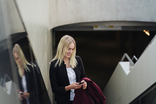 Blond businesswoman using smartphone while using escalator