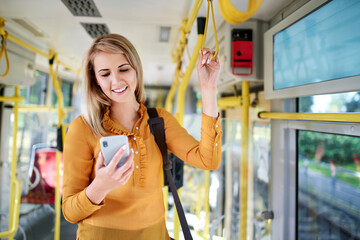 Wall Mural - Smiling young woman using smartphone in a tram