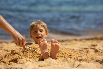 Canvas Print - Child, tickling sibling on the beach on the feet with feather, kid cover in sand, smiling, laughing