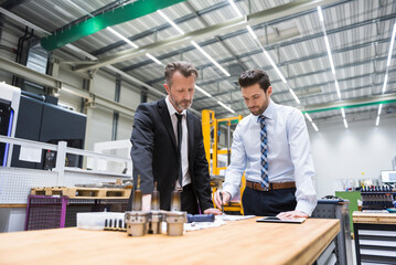 Two businessmen at table in factory shop floor examining product