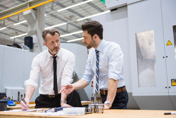 Canvas Print - Two businessmen at table in factory shop floor discussing