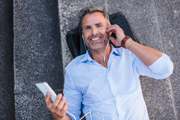 Wall Mural - Smiling man lying on stairs with cell phone and earbuds