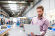 © tunedin - Young businessman using laptop in production hall