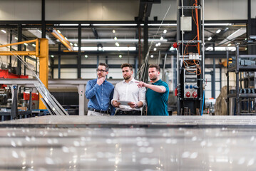 Three men sharing tablet on factory shop floor