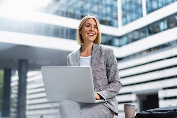 Poster - Smiling young businesswoman using laptop in the city