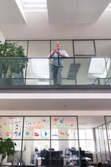 Sticker - Successful businessman standing at railing in his office, using smartphone