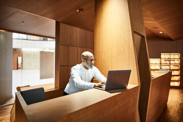 Wall Mural - Mature man working on laptop at workspace in library