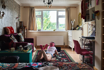 Sticker - Young woman with pink hair lying on carpet wearing headphones and using laptop at home