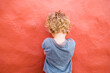© tunedin - Back view of little boy standing in front of red wall