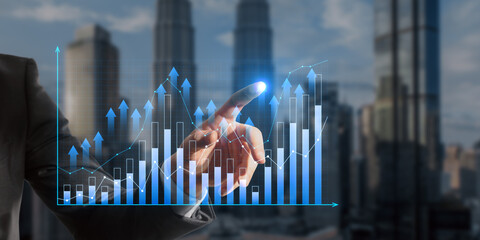 Close up of male hand pointing at growing business graph on blurry city background. Financial growth and technology concept. Double exposure.