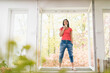 © tunedin - Smiling woman standing in kitchen on windowsill