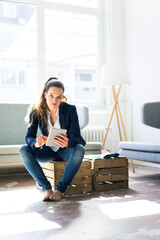 Poster - Businesswoman sitting on a crate using tablet