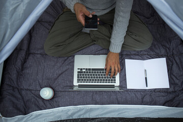 Poster - Man sitting in tent using laptop and cell phone, partial view