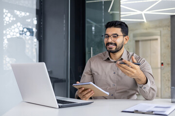 Business professional holding a notebook and engaging in a virtual meeting from a modern office environment.