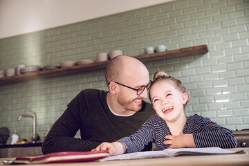 Father and daughter sitting in kitchen, doing homework