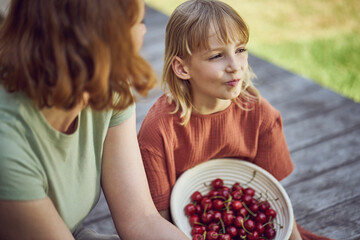 Wall Mural - Close-up of mother and daughter eating cherries while sitting in yard