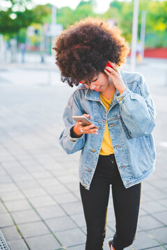 Young woman with afro hairdo using smartphone and headphones in the city