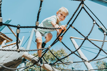 boy climbing on spider web in public park during sunny day