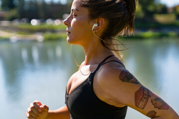 Wall Mural - Tattooed young woman with earbuds jogging at the riverside