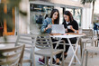 © tunedin - Two friends sitting together at a pavement cafe using laptop