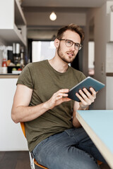 Wall Mural - Young man with tablet sitting in kitchen at home