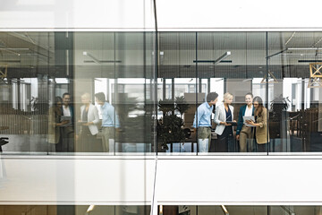 Canvas Print - Businesswoman and empoyees talking behind windowpane in office