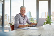 © tunedin - Portrait of smiling mature man using laptop on table at home