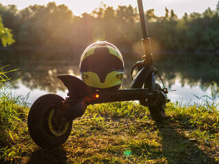 Wall Mural - A modern electric scooter in the park at sunset. Use a helmet for traveling . Summer time.