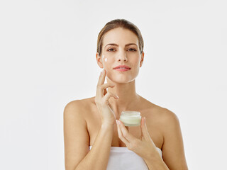 Portrait of smiling woman with cream pot applying moisturizer on her face