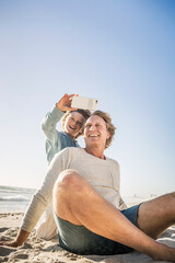 Wall Mural - Father having fun with his son on the beach, taking smartphone pictures