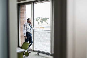 Wall Mural - Businessman looking at windowpane with world map in office