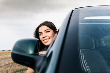 Poster - Smiling young woman leaning out of car window