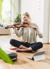 Wall Mural - Woman with tablet sitting on the floor at home playing violin