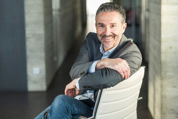 Wall Mural - Portrait of a smiling mature businessman sitting on chair in office